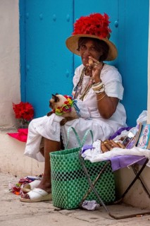 Old Cuban woman smokes a Cuban cigar on the street and posts with her cat for the tourists, La