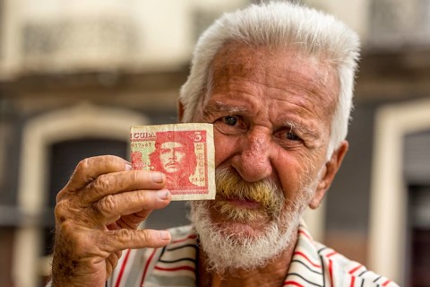 Old Cuban man holding a three peso banknote with the portrait of Ernesto Che Guevara in his hand,