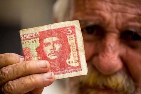 Old Cuban man holding a three peso banknote with the portrait of Ernesto Che Guevara in his hand,