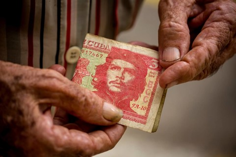 Old Cuban man holding a three peso banknote with the portrait of Ernesto Che Guevara in his hand,