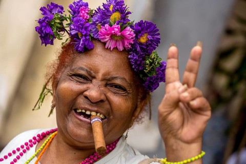 Peace sign, old Cuban woman with flowers and cigar posing for tourists for a tip, La Habana,