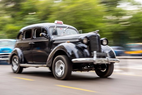 Speed, blurred, moving old car, black oldtimer in street scene, old american street cruiser on the