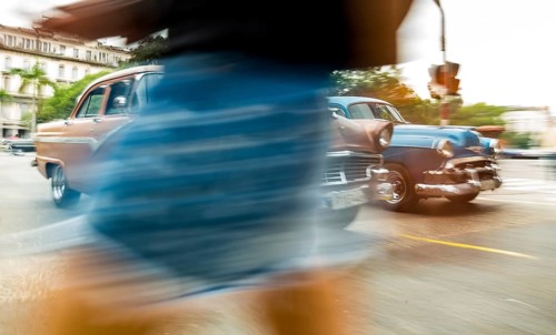 Part of a pedestrian in front of cars, speed, blurred, moving old car, vintage car in street scene,