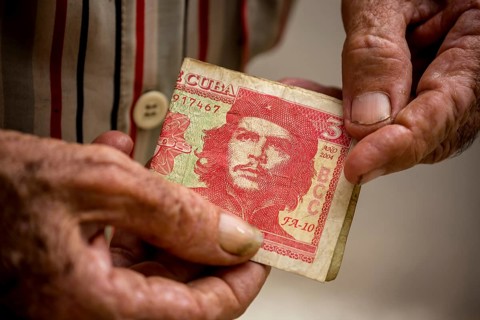 Old Cuban man holding a three peso banknote with the portrait of Ernesto Che Guevara in his hand,