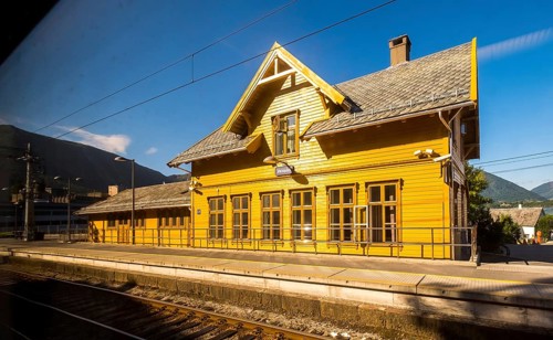 Yellow wooden railway station building Vaksdal, railway tracks, blue sky, near Bergen city railway