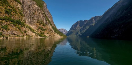 An approaching excursion boat on a beautiful fjord reflecting the light, surrounded by rocks partly