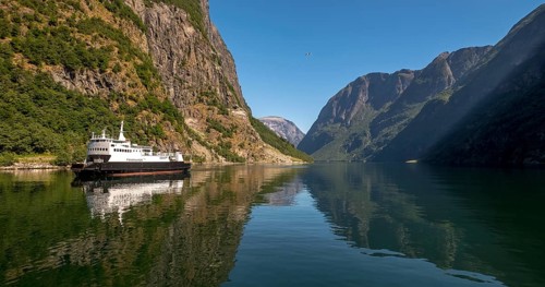 An approaching excursion boat on a beautiful fjord reflecting the light, surrounded by rocks partly