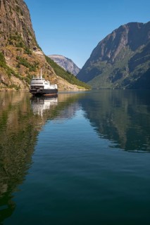 An approaching excursion boat on a beautiful fjord reflecting the light, surrounded by rocks partly