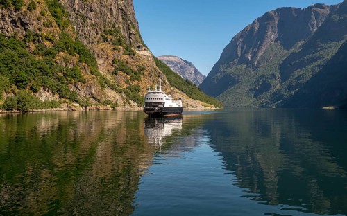 An approaching excursion boat on a beautiful fjord reflecting the light, surrounded by rocks partly