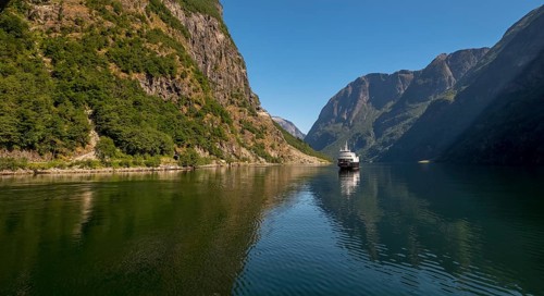 An approaching excursion boat on a beautiful fjord reflecting the light, surrounded by rocks partly