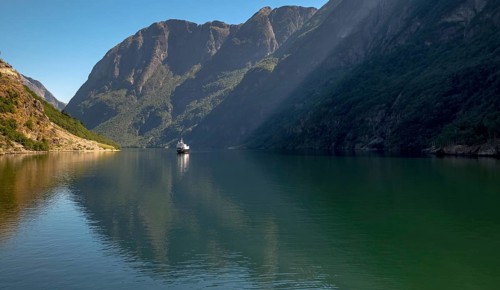 An approaching excursion boat on a beautiful fjord reflecting the light, surrounded by rocks partly