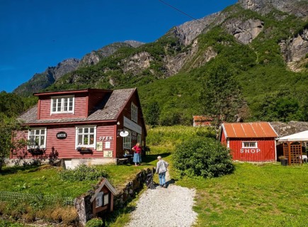 Tourists at mountain hut station, red wooden houses, gravel path, mountains, meadow, blue sky,