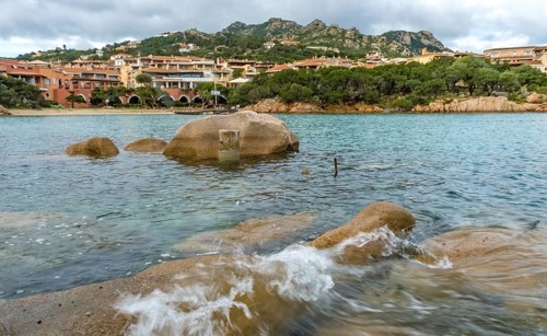 Sardinia, waves on the rocky coast, residential complex in the picturesque harbour town of Porto