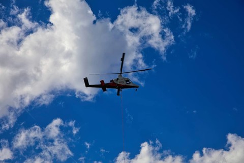 Small helicopter in the blue sky with few clouds, transport helicopter, timber transport, Saas