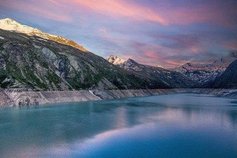 Early morning light over a lake with snow-covered mountains and pink sky, Mattmark reservoir, Saas