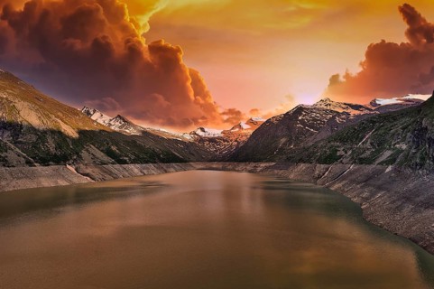 Mountain lake at sunset with dramatic clouds and orange sky, Mattmark reservoir, Saas Almagell,