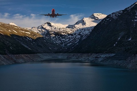 Aeroplane flying over a mountain lake with snow-covered peaks under a blue sky, Mattmark reservoir,