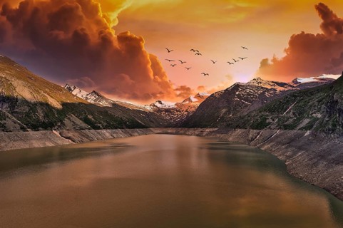 Dramatic sunset over a mountain lake with flying birds and clouds, Mattmark Reservoir, Saas