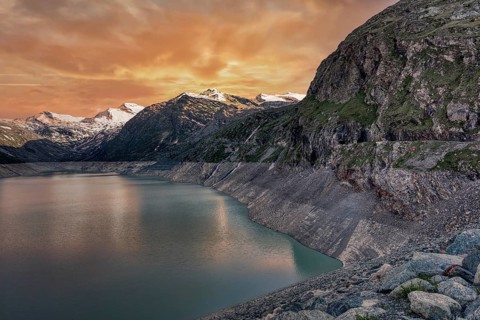 Sunset over a mountain lake with snowy peaks and rocky cliffs, Mattmark reservoir, Saas Almagell,