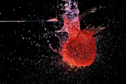 A red water balloon is penetrated by an arrow and creates a lively, powerful water scene,