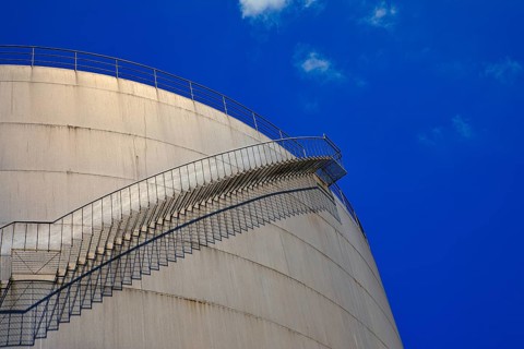 A staircase runs along a large tank in front of a deep blue sky, elevated tank, chemical, company,