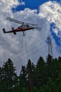A helicopter flies over a forest and transports a load next to power lines, transport helicopter,