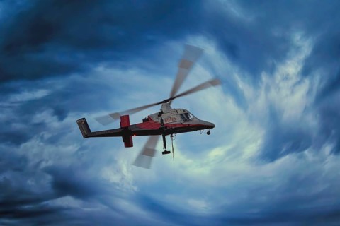 A helicopter flies through a dramatic, stormy blue sky, transport helicopter, timber transport,