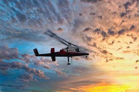 A helicopter flies in front of a colourful sunset with dramatic cloud formations, transport