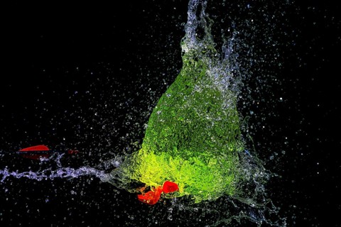 A green water balloon bursts and creates a dynamic water splash scene while an arrow penetrates it,