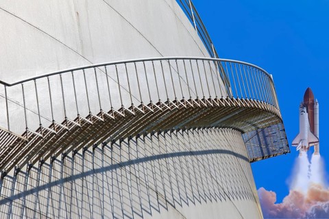 A rocket launches next to a large tank with a metal staircase in the foreground, elevated tank,
