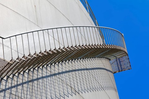 The staircase runs along a large tank in front of a clear blue sky, high tank, chemical, company,