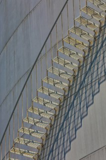 Close-up view of a metal staircase on an industrial gas tank with long shadow lines, elevated tank,