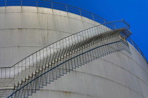 Large, curved metal staircase runs along a tank under a clear sky, elevated tank, chemical,