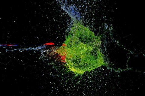 A green water balloon is pierced by an arrow and explodes in a dark, dynamic scene, high-speed