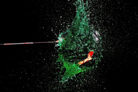 A green water balloon explodes under the impact of an arrow against a dark background, high-speed