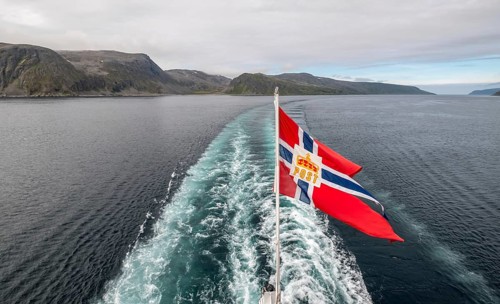 The post symbol on a Norwegian flag of a Hurtigruten ship, foaming spray, Honningsvåg, Finnmark,
