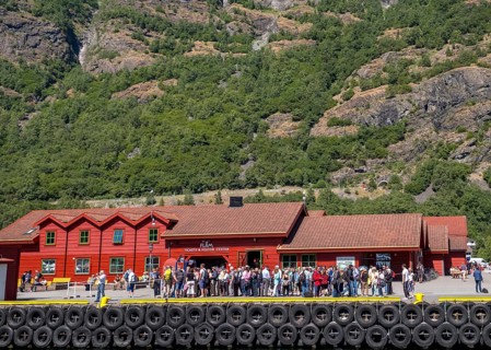 Flåm, tourists at the TICKETS & VISITOR CENTER, red wooden house, landing stage for ships, rock