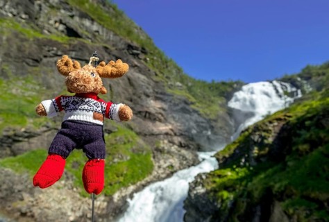Kjosfossen waterfall, mascot moose in front of waterfall, mountain, rock faces, meadow, sky,