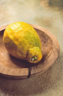 A vibrant lemon sits on a rustic wooden plate, showcasing its uneven texture and vivid color. The