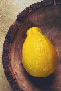 A vibrant yellow lemon sits alone in a wooden bowl with a rough rim, highlighting its natural