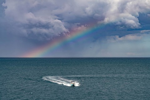 Rainbow over the Adriatic Sea and motorboat near Polignano a Mare, Apulia, Italy