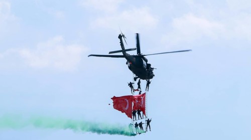 Türkiye special operations police hang from a helicopter with ropes, carrying weapons and unfurling