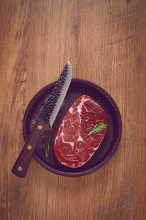 Steak made from fresh beef, with herbs and various spices, in a clay pan, with a kitchen knife,