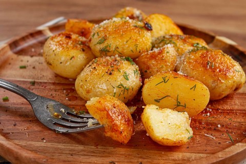 Half-eaten fried new potatoes, with butter and dill, on a wooden plate, with a fork, at home,