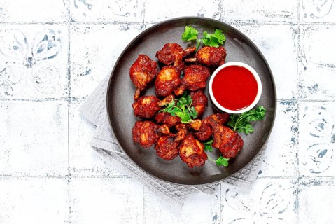 Crispy pieces of fried chicken, on a plate with sauce and herbs, in a modern kitchen environment,