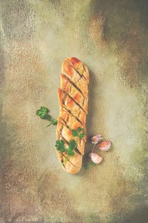 Garlic bread, baguette with garlic butter and herbs, with herbs and garlic cloves
