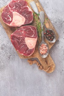 Freshly sliced beef legs, two ossobuco steaks, on a wooden board, with spices and herbs, ready to