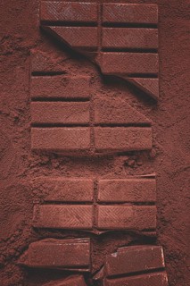 Chocolate bars broken and scattered on cocoa powder background with rich texture and color