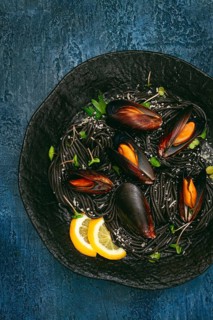 Spaghetti with black squid, black pasta, with boiled mussels, on a black plate, with parsley and