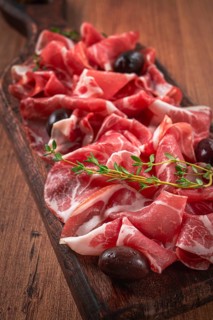 Freshly cut dried meat, served with olives and herbs, on a wooden chopping board, no people